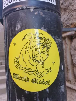 Street sticker Yellow circular sticker with a line drawing of a dog's head with the Earth in its mouth, surrounded by a chain. The text "World Global" is written below the image.