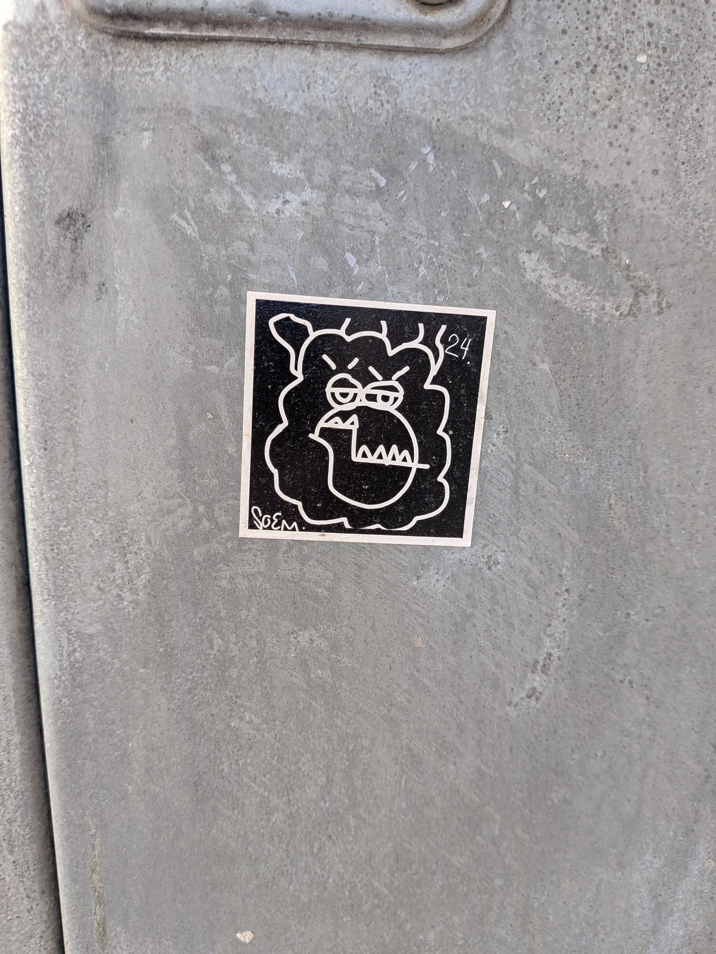 A square-shaped sticker featuring a stylized, angry-looking face or creature in white outline against a solid black background. The character has furrowed brows, narrow eyes, and an open mouth revealing sharp, triangular teeth. Its head is surrounded by a wavy, cloud-like or shaggy outline. A thin white border frames the design. The text 'SoEM' is visible in the bottom left corner, and '24.' is in the top right.