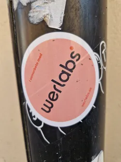 Street sticker A round, peach-colored sticker with the word 'Werlabs' in bold, black text.  The smaller text on the sticker says 'I samarbete med' (In collaboration with) and the website werlabs.se.  The sticker appears to be on a dark-colored pole.
