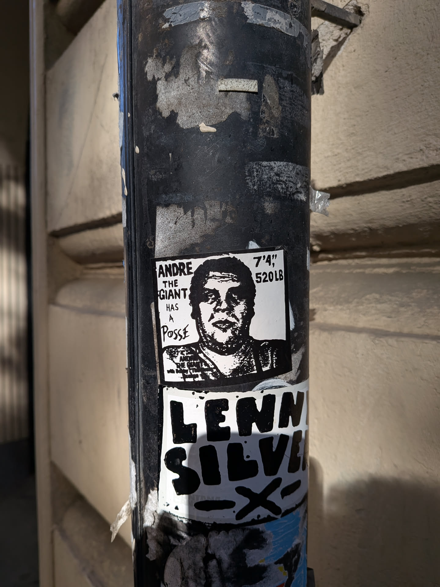 The sticker features a black and white illustration of Andre the Giant's face. To the right of his face, text reads '7'4" 520LB'. Below the portrait, the words 'ANDRE THE GIANT HAS A POSSE' are printed. The sticker appears to be printed on paper and is adhered to a dark, weathered pole, overlapping with other stickers.