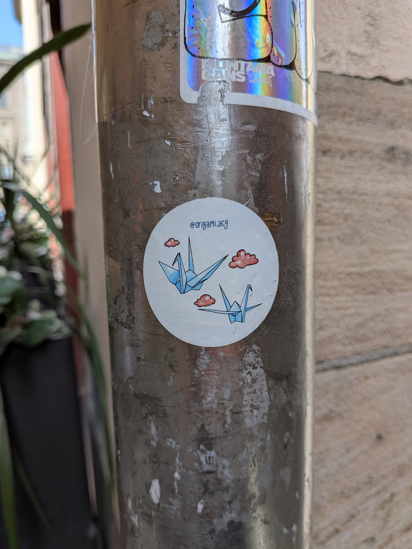 A round white sticker depicting two light blue origami cranes flying amidst three small, stylized red clouds. The Instagram handle '@origami.acg' is printed in blue at the top.