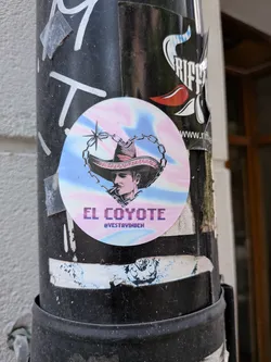 Street sticker A circular sticker with a pastel pink and blue iridescent background. It depicts a black-and-white illustration of a man in a sombrero framed by a heart-shaped chain. Below the image, the text 'EL COYOTE' and the handle '@VESTAVINDEN' are displayed.