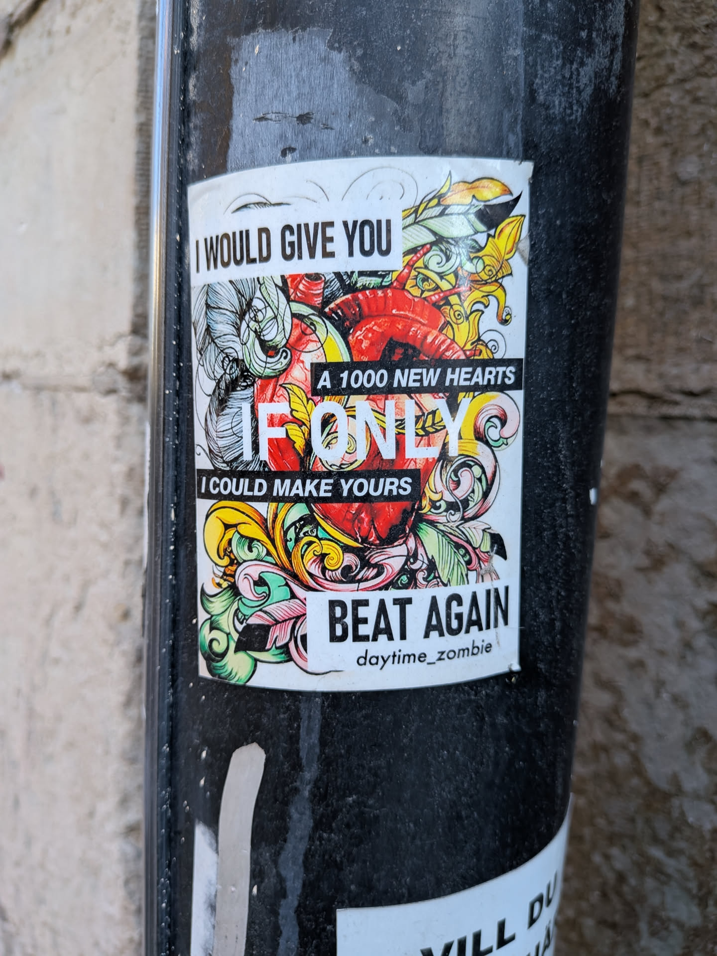 A rectangular sticker featuring a central, stylized anatomical heart rendered in red, surrounded by an intricate explosion of swirling, organic, and feather-like patterns in vibrant shades of yellow, green, blue, and pink. The design is outlined in black on a white background. Bold, blocky text overlays the illustration, conveying a melancholic message. The sticker is applied to a dark, textured pole, showing slight wear around its edges.