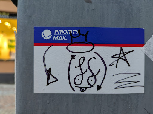 Street sticker A Priority Mail shipping label has been repurposed as a canvas for a fun, quirky drawing.  The doodle depicts a character with a crown and what seems to be a playful expression. There are additional markings such as a star and squiggles around the main figure.  The sticker is affixed to a grey metal surface.