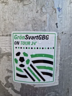 Street sticker A sticker featuring the text 'GrönSvartGBG ON TOUR 24' and a graphic design with a soccer ball and green and black stripes. The sticker appears to be affixed to a weathered surface, with water droplets visible on its surface.