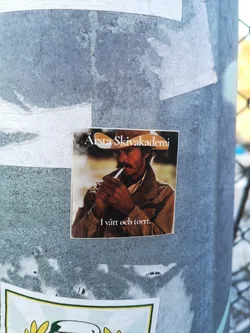 Street sticker The sticker features a close-up, sepia-toned portrait of a man with a prominent mustache, wearing a cowboy hat and a collared jacket. He is holding a lit cigarette to his mouth, with a wisp of smoke visible. The lighting suggests a backlight, highlighting the contours of his hat and face. The overall aesthetic is reminiscent of vintage photography or film stills. White text is overlaid on the image, with 'Årsta Skivakademi' at the top and 'I vått och torrt.' at the bottom.