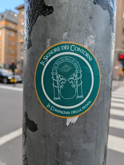 Street sticker Circular teal sticker with a yellow border. It depicts a white line-art illustration of the Doors of Durin. Italian parody text reads 'IL SIGNORE DEI CONTORNI' and 'LA COMPAGNIA DELLA PATATA'.