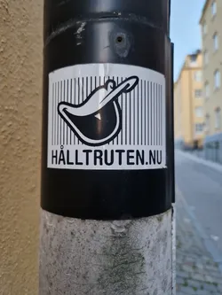 Street sticker Black and white sticker with a cartoon-like image of a hat and the website address Hälltruten.nu. The sticker is affixed to a grey pole.