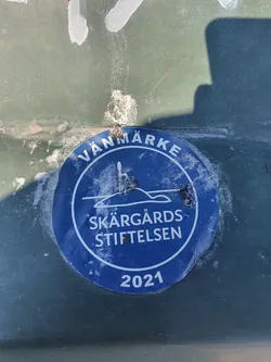 Street sticker A blue round sticker with the text "Vänmarke Skärgårds Stiftelsen 2021" and a picture of an island with a lighthouse.  The sticker appears to be weathered.