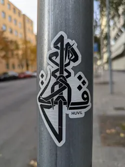 Street sticker A sticker featuring a bold, black and white abstract design. The style is geometric and minimalist, with sharp lines and shapes creating an intricate pattern.  A small text 'HUVIL' is visible at the bottom of the sticker. The sticker is affixed to a gray metal pole.