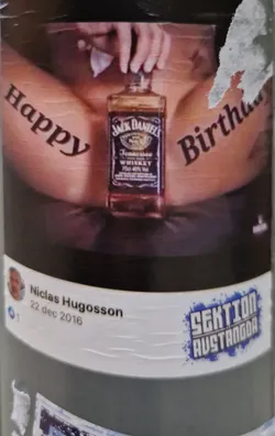 Street sticker A sticker featuring a suggestive image of a person holding a bottle of Jack Daniel's Tennessee Whiskey with the words "Happy Birthday" tattooed on their body.  The sticker also includes a social media post crediting Niclas Hugosson and mentioning Sektion Austangda.