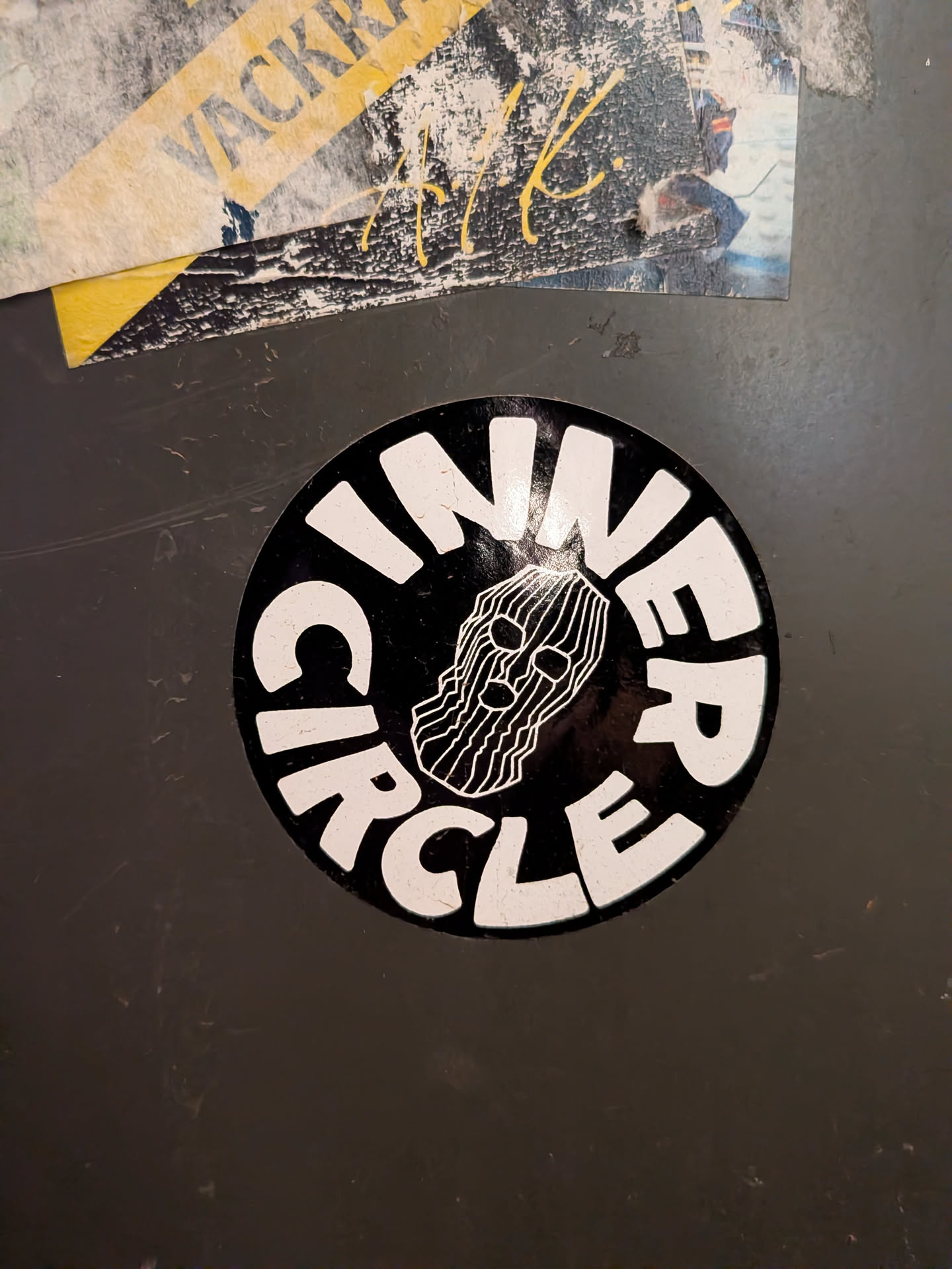 The sticker is circular with a black background. In the center, a stylized skull wearing a balaclava is depicted with white, thin, parallel lines representing the fabric. The words 'INNER CIRCLE' are written in bold, white, sans-serif capital letters, arching around the top and bottom of the skull image, forming a complete circle. The overall aesthetic is stark and graphic.