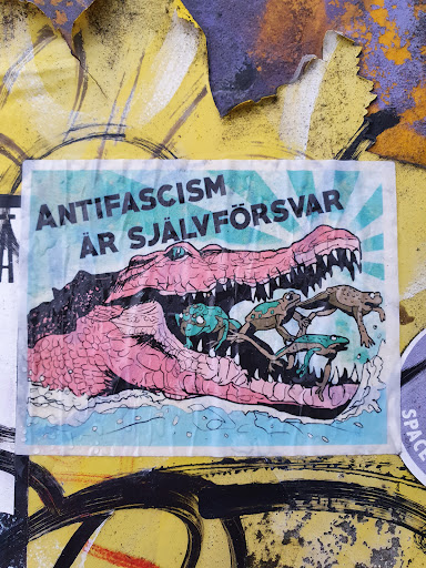 Street sticker A sticker with an illustration of a crocodile with frogs in its mouth. The text on the sticker says "Anti-fascism är självförsvar" which translates to "Anti-fascism is self-defense" in Swedish.