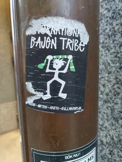 Black and white sticker with a stick figure holding a green and white scarf. The text 'International Bauen Tribe' is written at the top, and locations 'Söder, öster, Årsta, Gullmarsplan' at the bottom.