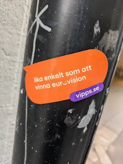 Street sticker An orange sticker on a black pole features the text 'lika enkelt som att vinna euro:)vision' and the website 'vipps.se'.