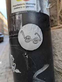 A round sticker on a pole features a simple black line drawing of glasses with smiling eyes inside the lenses.