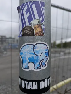 Street sticker A cute elephant sticker with a white border and a blue water pattern filling its body. The sticker is placed on a grey pole.