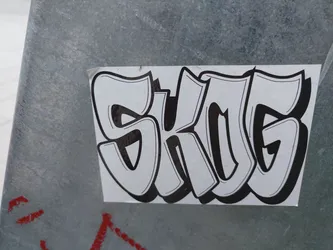 A sticker with a graffiti-style depiction of the letters "SKG" in bold, black outlines on a white background.