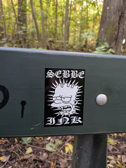 Street sticker The sticker is black and white, featuring a stylized depiction of Bart Simpson from The Simpsons. His hair is depicted as spiky rays emanating from his head, and he has a wide, aggressive grin with his tongue sticking out. Above Bart's head, in a gothic-style font, is the word 'SEMME'. Below Bart's head, also in a gothic-style font, is the word 'INK'. The overall impression is edgy and punk-inspired.