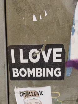 A black and white sticker with the text "I LOVE BOMBING" on a cracked surface. The sticker shows signs of wear and tear.