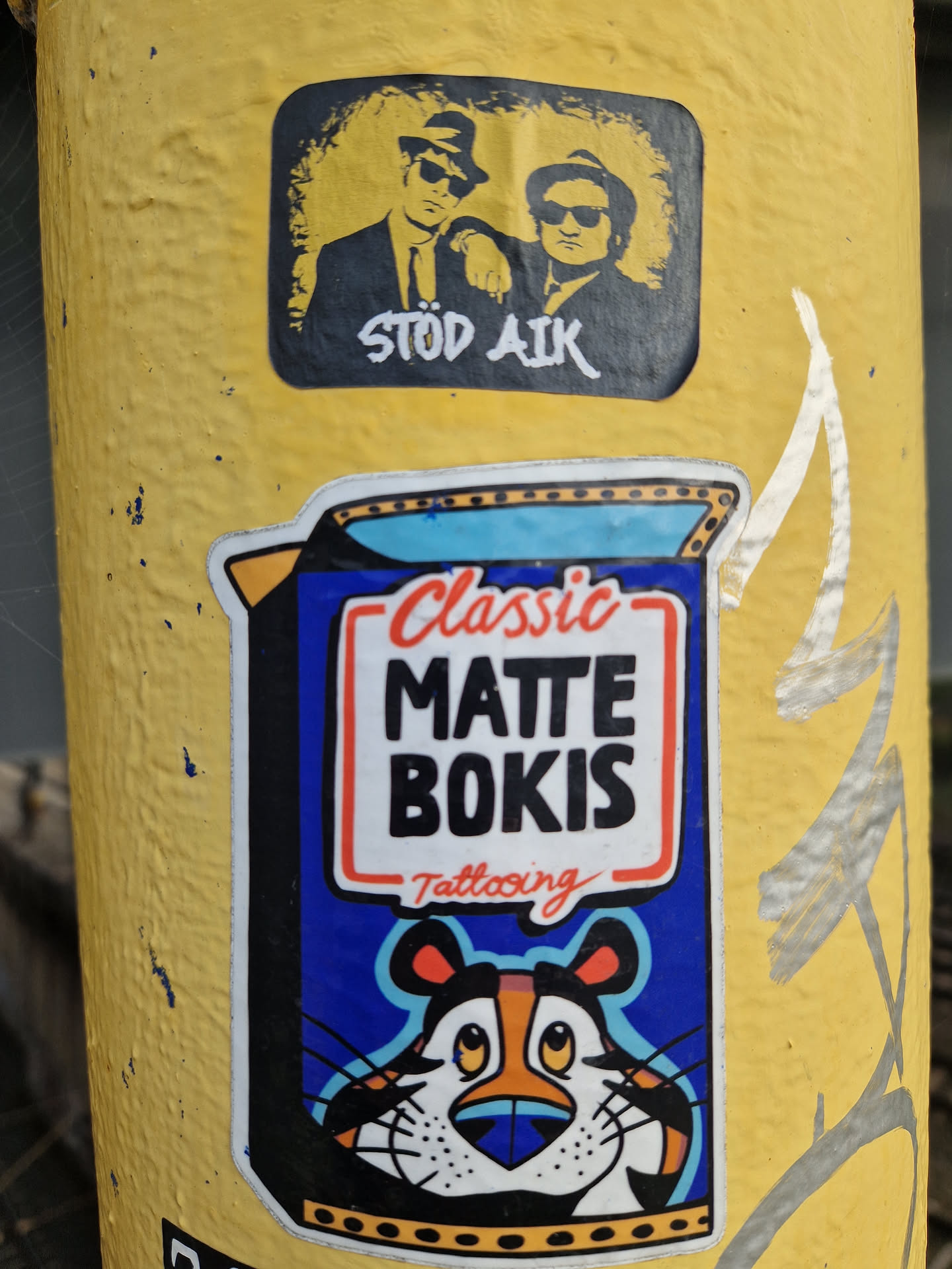 A colorful sticker designed to look like a Kellogg's Frosted Flakes cereal box. It features a blue background with a white rectangular label outlined in red, containing the text 'Classic MATTE BOKIS Tattooing'. Below the text is an illustration of a cartoon tiger resembling Tony the Tiger, with orange, black, and white fur, a blue nose, and large eyes looking upwards. The sticker has a white die-cut border.