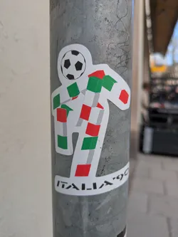 Street sticker The sticker shows the Italia '90 World Cup mascot, a white figure with a soccer ball for a head and a body constructed of red, white, and green cubes, resembling the Italian flag.  The words 'ITALIA '90' are printed below the figure.