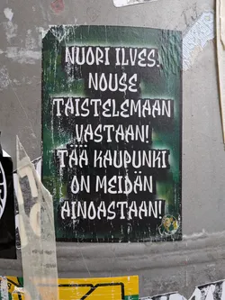 A rectangular sticker featuring bold white text in a stylized, slightly runic font against a dark green and black background. The background has a spray-painted, textured look. In the bottom right corner, there is a small circular emblem featuring the green and yellow colors of the Ilves sports club. The sticker shows some wear and tear, particularly around the edges.