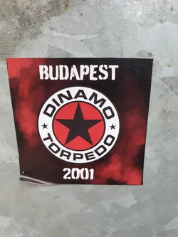 A sticker featuring a red and black logo with the text 'Dinamo Torpedo' and 'Budapest 2001'. The design has a star in the center and a smoky background.