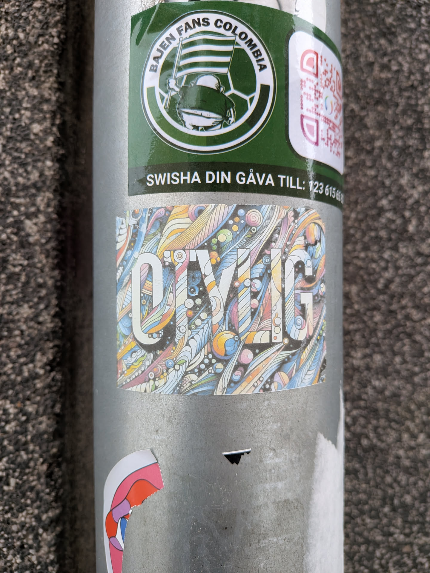 Street sticker The central sticker is a rectangular piece featuring the word "OIVLIG" in large, white, sans-serif letters. The background and the interior of the letters are filled with a dense, intricate pattern of swirling lines, organic shapes, dots, and small circles. The color palette is vibrant and diverse, including shades of blue, orange, yellow, pink, purple, and green, creating a psychedelic or dreamlike effect. The overall style is highly detailed and illustrative, with a hand-drawn feel, and the sticker shows minor signs of wear.