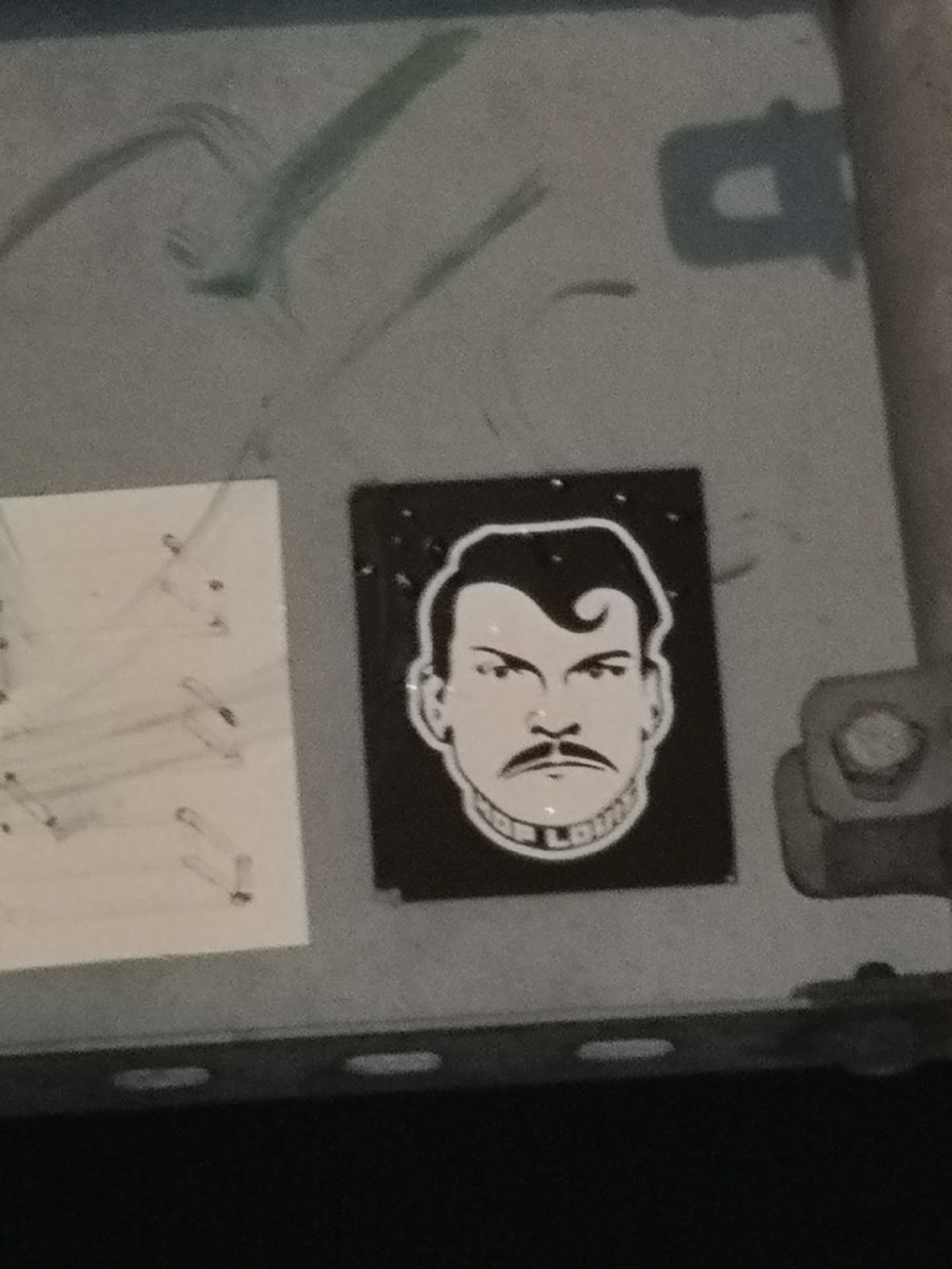 The sticker is rectangular with a black background, featuring a stylized, high-contrast portrait of a man's head and shoulders. The man has a strong jawline, a prominent handlebar mustache, and slicked-back hair with a distinctive curl or pompadour on the forehead. His eyes are narrow and intense, conveying a determined or stern expression. The entire figure is rendered in white outlines and fills against the black background. Around the base of his neck, forming a collar-like shape, is the text "JOE LOUIS" in white capital letters. Small white dots are scattered in the black background, resembling stars or a textured effect.