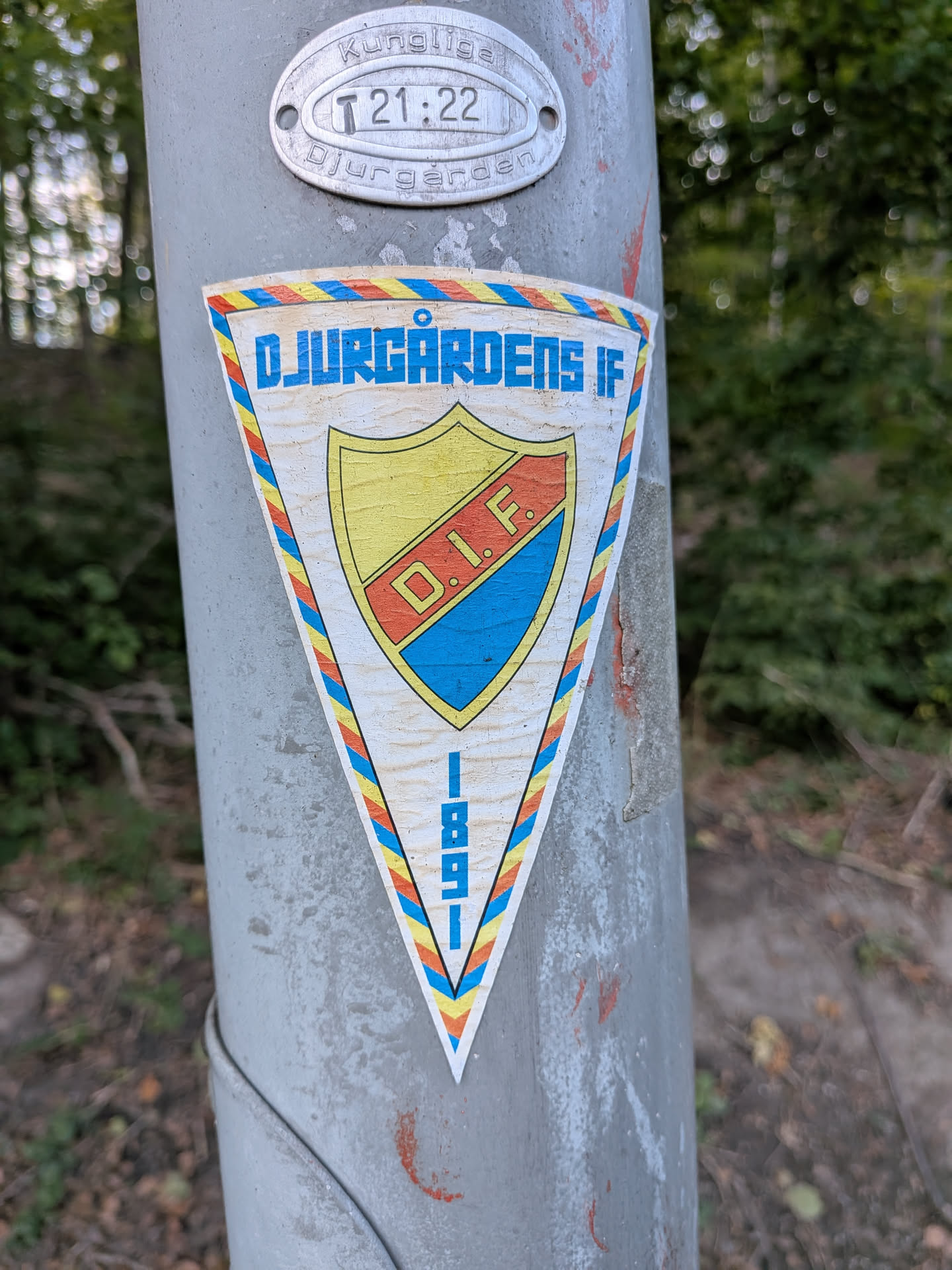 The sticker is triangular in shape with a white background. It features a crest with yellow and blue sections divided by a red band. Within the crest are the letters 'D.I.F.' in red. The outer edge of the sticker has a border with a repeating pattern of red, yellow, and blue diagonal lines, enclosed by a thin black outline. At the bottom of the sticker, oriented vertically, are the numbers '1 8 9 1' in blue.