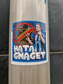 Street sticker A sticker featuring a football player with a crossed-out logo. The text 'Hata Gnaget' is prominently displayed. The sticker appears to be expressing dislike towards a particular football team or organization.