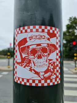 A red and white checkered sticker with a skull wearing a hat and sunglasses and smoking a cigarette. The text on the hat says "FCERBGC".
