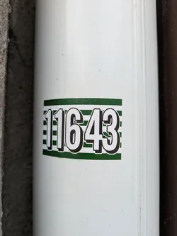 Street sticker A close-up shot of a white sticker with the number 11643 printed in bold, black text on a green and white striped background.  It's affixed to a white cylindrical surface, possibly a pipe or column.