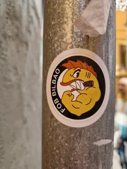 Street sticker This is a round sticker featuring a cartoon illustration of a muscular yellow fish with orange fins, smoking a cigar and flexing its bicep. The text "FOB BILBAO" is written around the fish in a circular pattern.