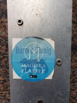 Round blue sticker with the text "Bätmer Musik" and a stylized letter M in the center. Below it, it says "Magiska Platser" and features an Apple App Store logo. The design includes a star and a map-like image.