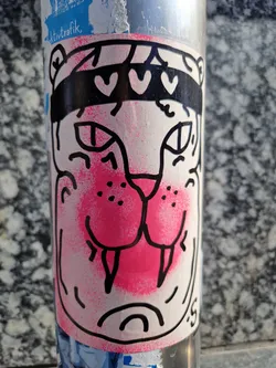 Close-up of a sticker featuring a stylized tiger's face. The tiger is depicted with a pink nose and mouth, black outline, and a black headband adorned with three white hearts. The style is simple and playful.
