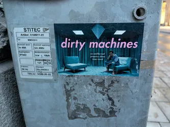 Street sticker The sticker features a surreal scene with a dark, teal-colored backdrop of draped curtains and a diamond-shaped geometric element at the top. In the foreground, two minimalist, teal-colored chairs are placed on a dark, textured floor. A person in a grey outfit is seated on one of the chairs, looking contemplative. The text 'dirty machines' is prominently displayed in a large, pink, sans-serif font across the upper portion of the sticker, with smaller text below reading 'an intellectual property about time travel'.