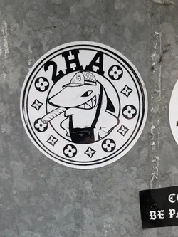 Street sticker Black and white sticker of a shark wearing a hat and smoking a cigar. The design is surrounded by a circular border with repeating Louis Vuitton-style flower patterns and the text "2HA".