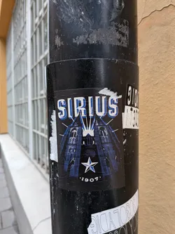 Street sticker A rectangular black sticker depicting a blue-toned illustration of Uppsala Cathedral's twin spires. The word 'SIRIUS' is displayed at the top in bold, blue-and-white block letters with light rays emanating from behind. A blue and white five-pointed star sits above the year '1907' at the bottom.