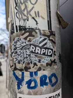 Street sticker The sticker features a detailed depiction of a Native American chief wearing a traditional headdress, positioned next to the word "Rapid" enclosed in a circular emblem, against a camouflage background. The design gives a unique blend of cultural symbolism and modern design elements.