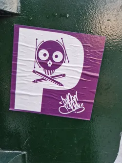 Street sticker A sticker featuring a purple skull with pencils crossed behind it. The skull is wearing drumsticks. The sticker is predominantly purple and white, with a white background and purple skull design.  There is a signature in white on the bottom of the purple area. 