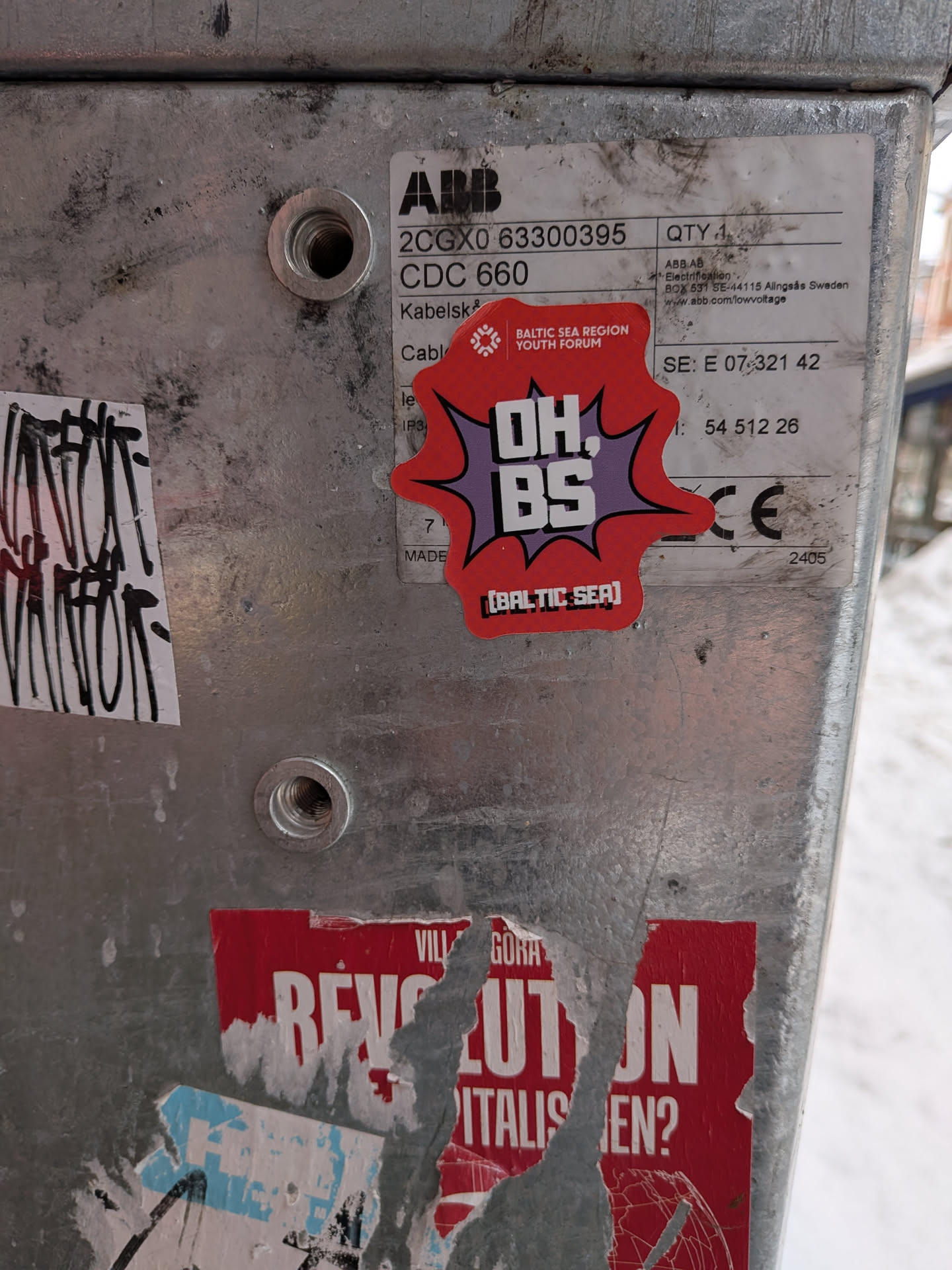 Street sticker The sticker is an irregularly shaped, vibrant red starburst or speech bubble design, outlined in black. It features a purple inner burst, against which the main text 'OH. BS' is prominently displayed in large, bold white letters with a black outline, in a comic book style font. Above this, in smaller white text, is 'BALTIC SEA REGION YOUTH FORUM' accompanied by a small, stylized logo resembling a snowflake or star. Below the main text, in white bracketed text, is '[BALTIC SEA]'. The sticker has a dynamic and impactful visual style.