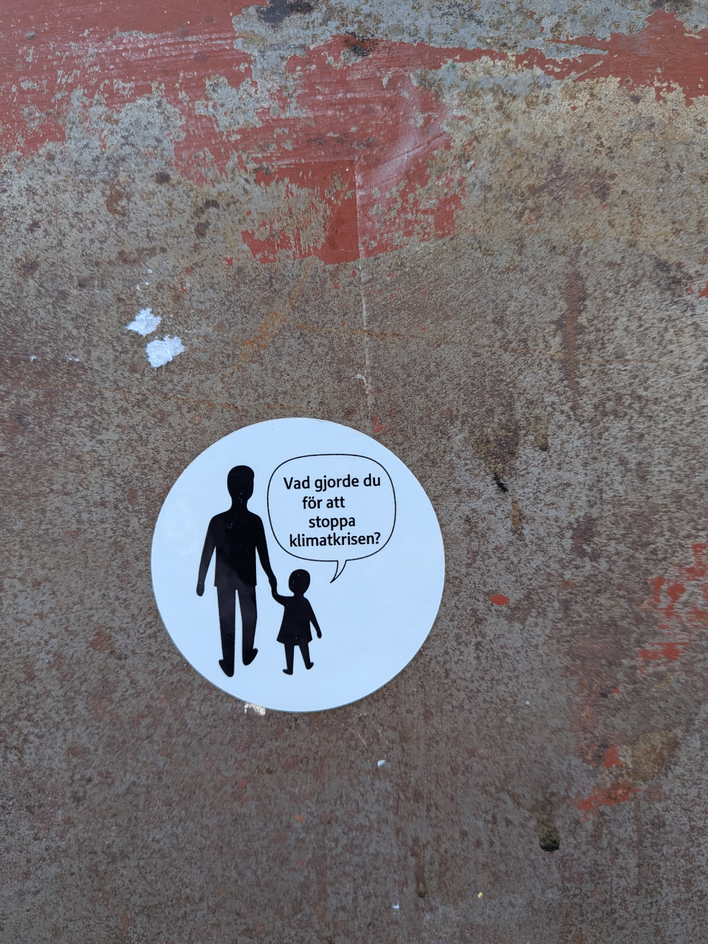 A circular, white sticker featuring two black silhouettes: an adult figure on the left holding hands with a smaller child figure on the right. A speech bubble originates from the child, containing black text. The design is stark and minimalist, using only black and white to convey a powerful message.
