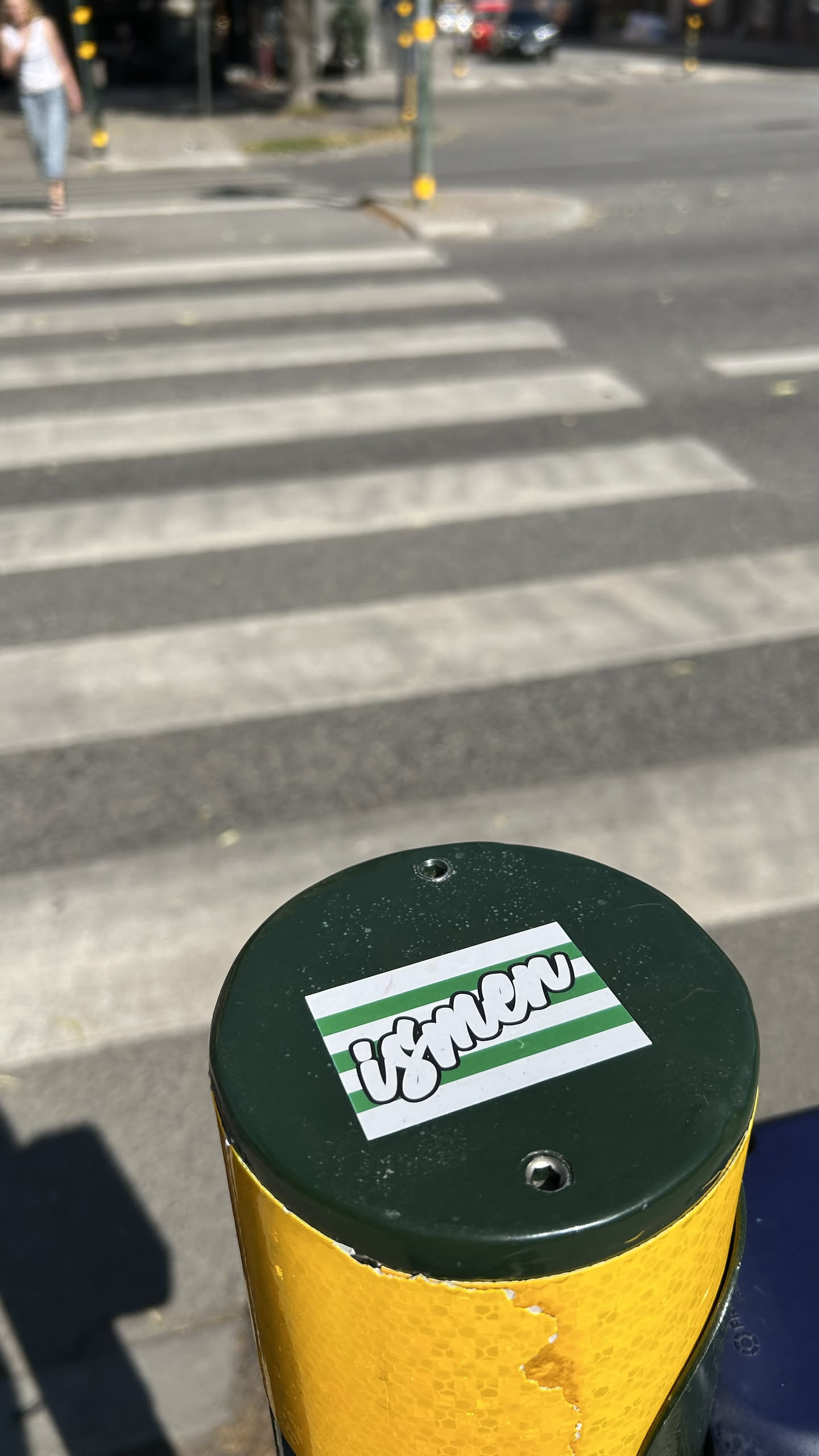 A rectangular sticker featuring the word 'ismen' in white bubble letters with black outlines, set against a background of alternating green and white horizontal stripes.