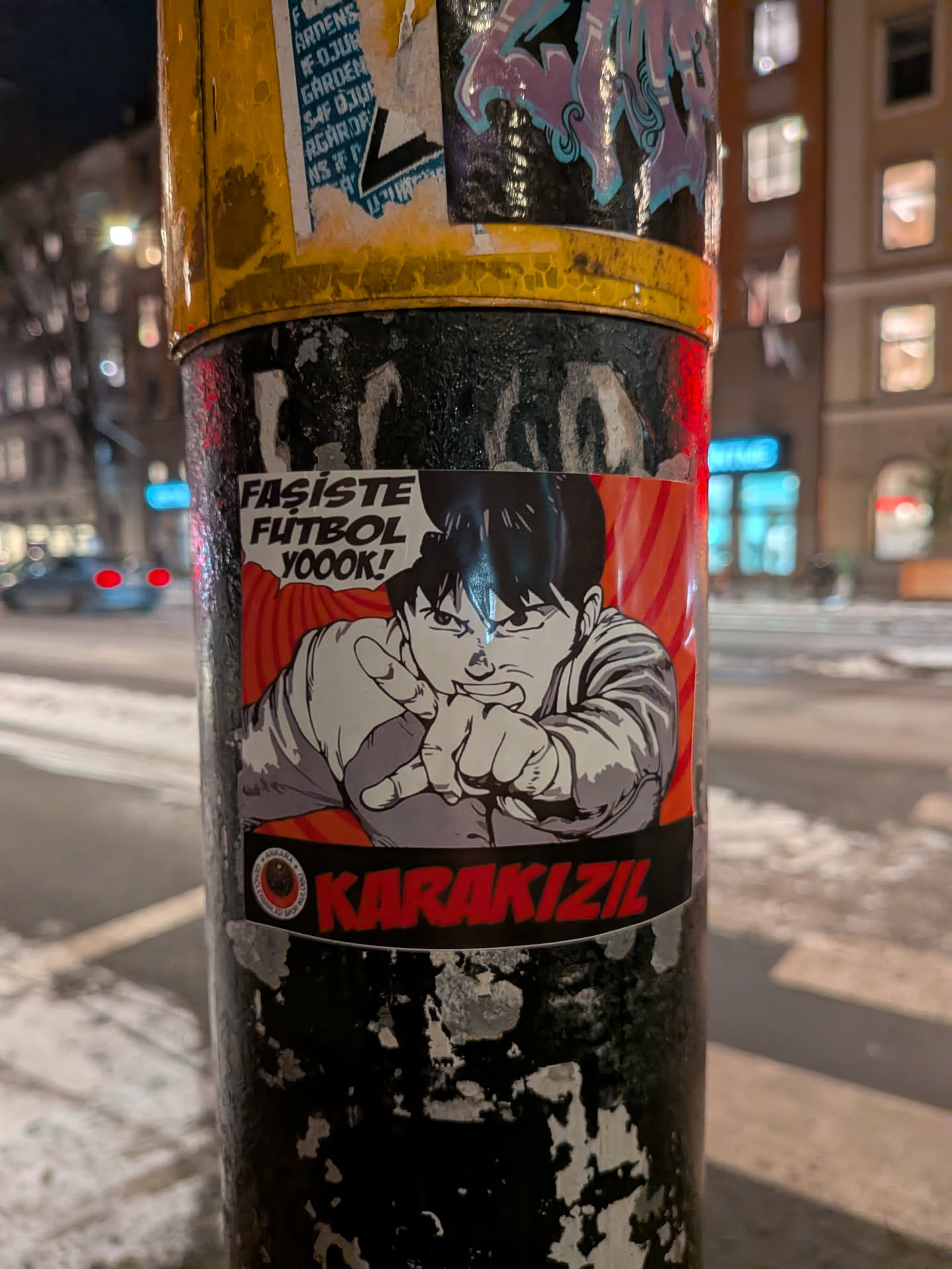 Street sticker The sticker features a dynamic manga/anime-style character, a young man with dark spiky hair and an angry, determined expression. He is depicted in a light-colored long-sleeved shirt, pointing directly forward with both hands. Above him, a black speech bubble contains the white text 'FASİSTE FUTBOL YOOOK!'. The background behind the character is a vibrant red with subtle diagonal darker red stripes. At the bottom of the sticker, a black banner displays the bold red text 'KARAKIZIL'. To the left of 'KARAKIZIL', there is a small circular logo in red, black, and white, which appears to contain the text 'ANKARA KARAKIZIL SPOR KULÜBÜ'. The overall aesthetic is bold and impactful, using strong contrasts and a classic comic book style.