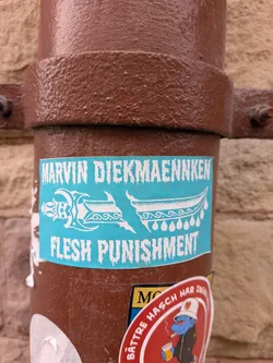 Street sticker A rectangular turquoise sticker stuck to a brown pipe. The sticker features white text in a dripping, distressed font. The top line reads 'MARVIN DIEKMAENNKEN' and the bottom line reads 'FLESH PUNISHMENT'. In the center is a white illustration of an ornate, stylized dagger broken into two pieces. The hilt on the left has decorative curves and a skull-like face, while the curved blade on the right features wave patterns and hanging teardrop shapes.