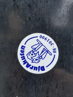 Street sticker A circular sticker with a white background and blue graphics. The central image features two stylized animal heads, possibly a dog and a cat, hanging upside down from a horizontal bar. They are depicted with simple line art, dots for eyes, and small ears. The text 'Djurakuten' is written in an arc along the bottom left edge of the circle, in blue uppercase letters. Along the top right edge, the number '08-301900' is written in a similar blue, uppercase font, also in an arc. A thin blue line forms a partial inner border around the design. The sticker appears slightly worn or dirty on a dark, textured surface.