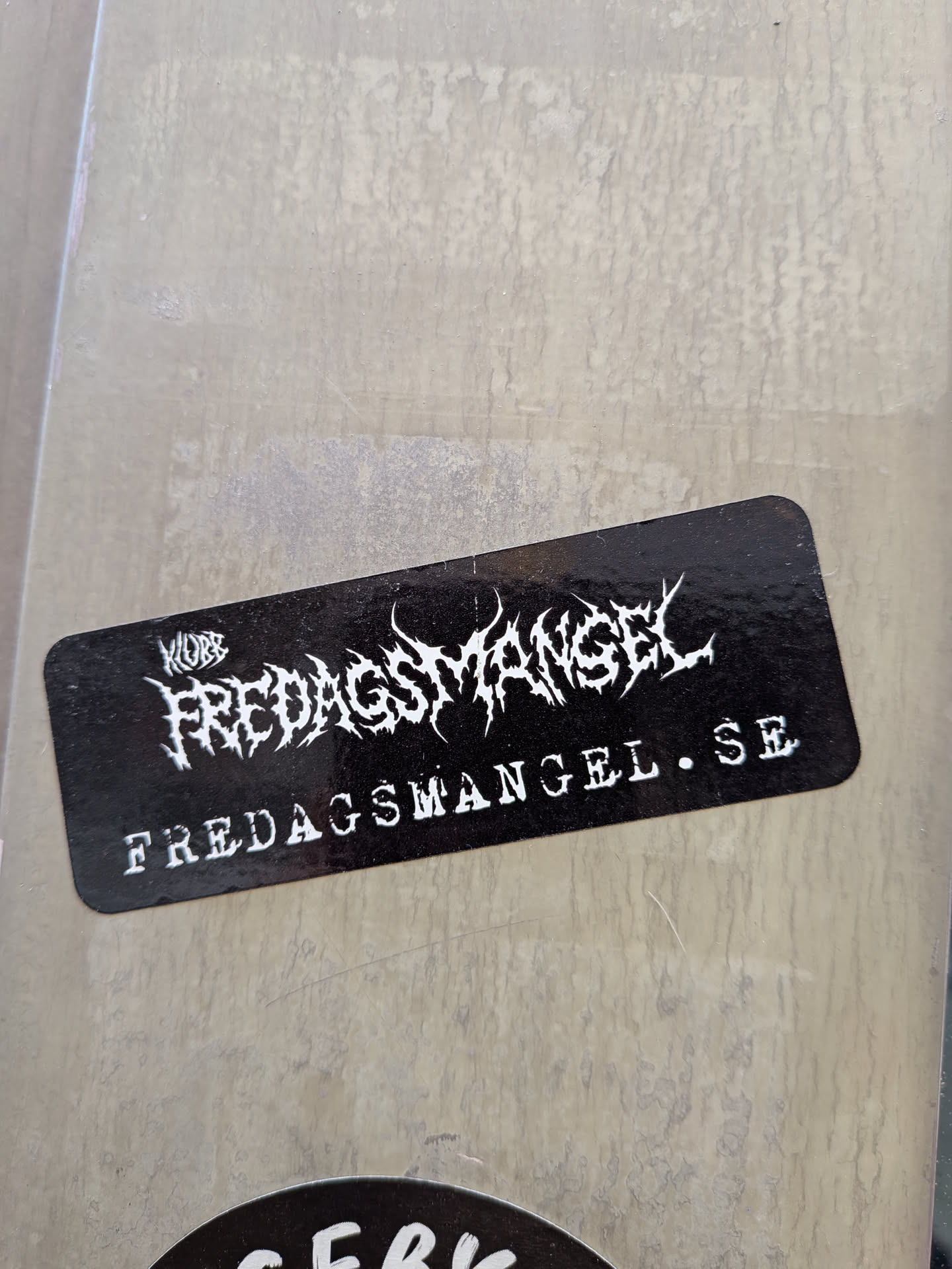 A rectangular black sticker with rounded corners. Features white, spiky death-metal style typography reading 'KLUBB FREDAGSMANGEL' and the website 'FREDAGSMANGEL.SE' below.