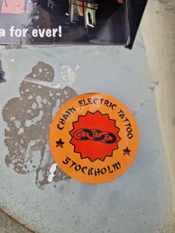 Street sticker Orange circular sticker with black text and logo.  The text reads: "Chain Electric Tattoo Stockholm". The logo is a stylized chain link. 